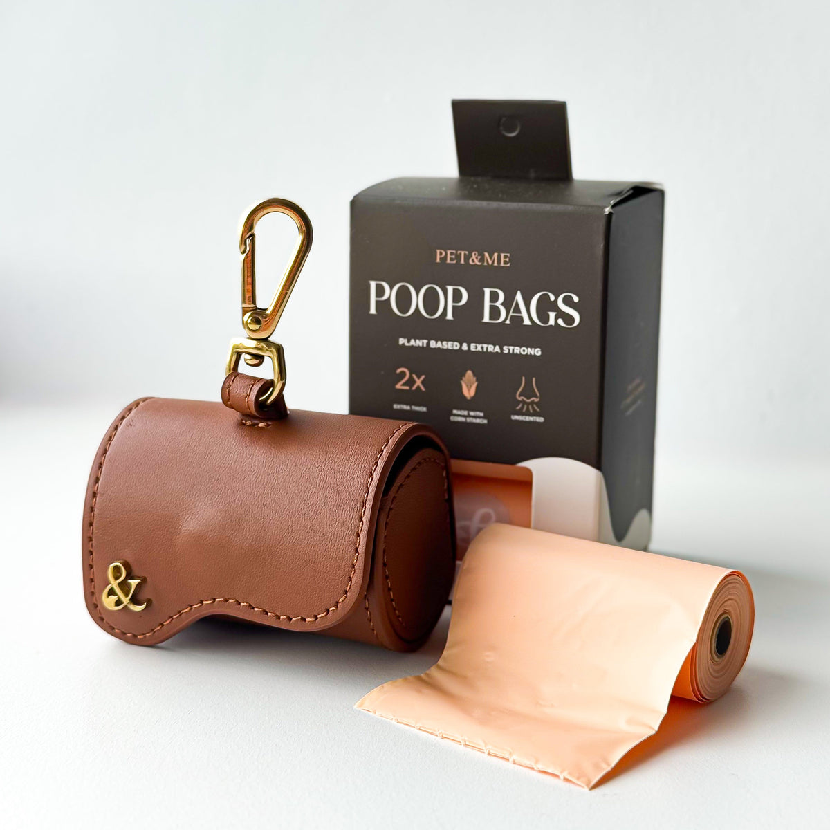 Brown leather poop bag holder with gold clip next to PET & ME compostable poop bags