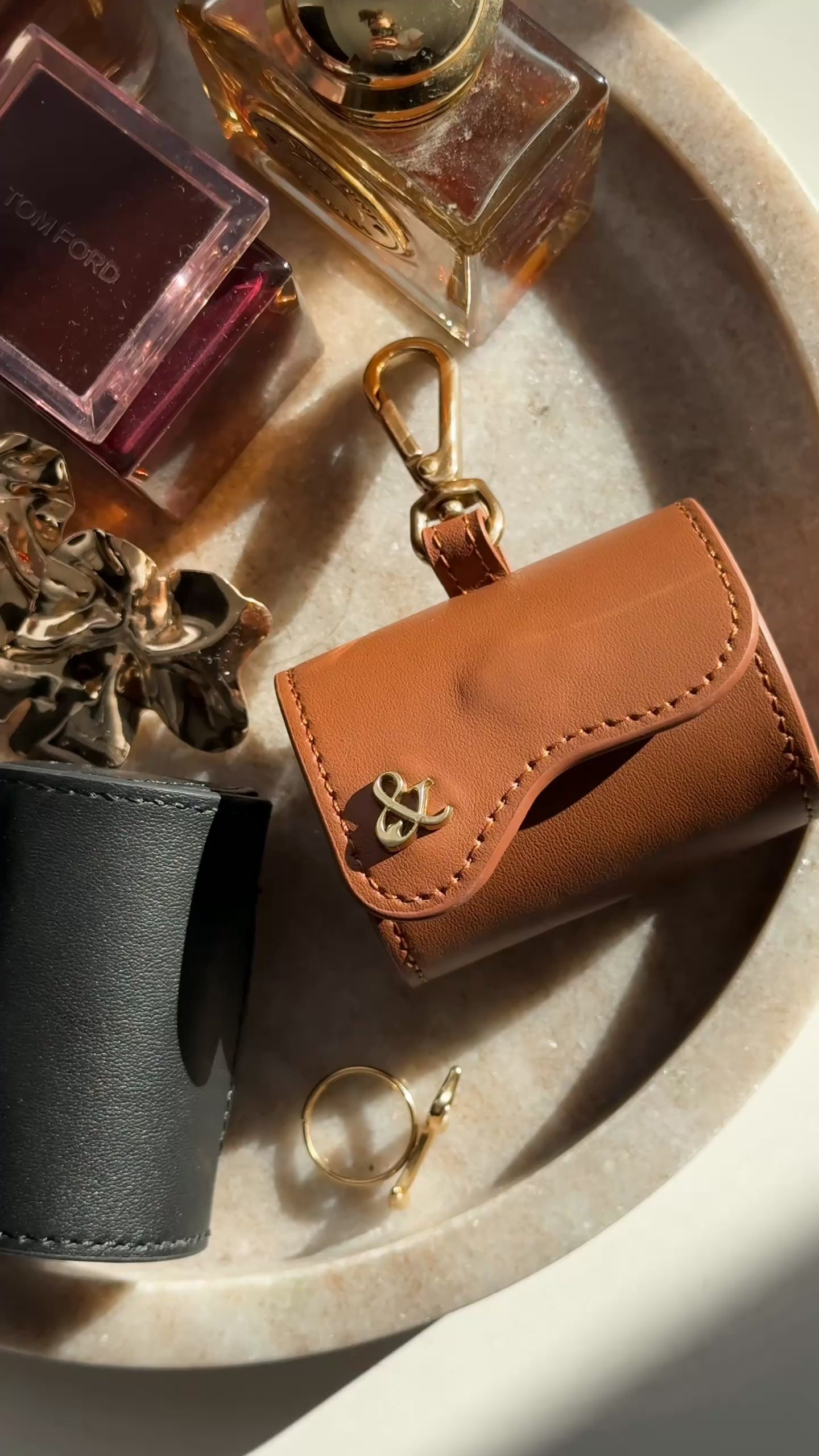 Brown and black leather poop bag holders with gold ampersand detail styled on a marble tray